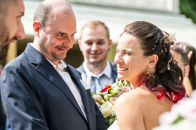 Coppia di sposi si abbraccia sorridendo, circondata da invitati e vegetazione lussureggiante presso Villa Luppis.