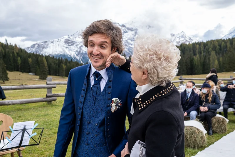 Un uomo in abito elegante sorride mentre conversa con una donna in un ambiente montano durante una cerimonia di...