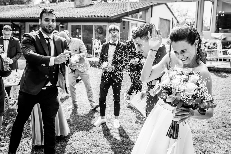 Coppia di sposi festeggia all'aperto mentre gli invitati lanciano petali di fiori e riso.