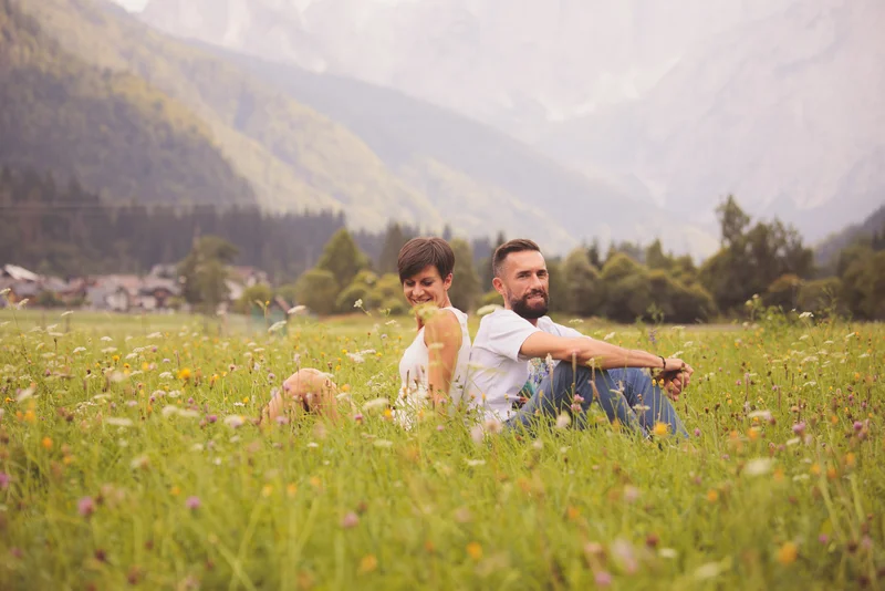 Coppia felice seduta su un prato fiorito, immersa nella natura montana.
