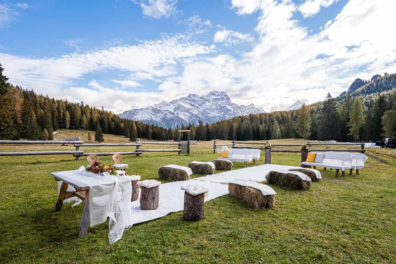 Allestimento per cerimonia all'aperto con vista montagna a Cortina, tavoli e sedute in legno.