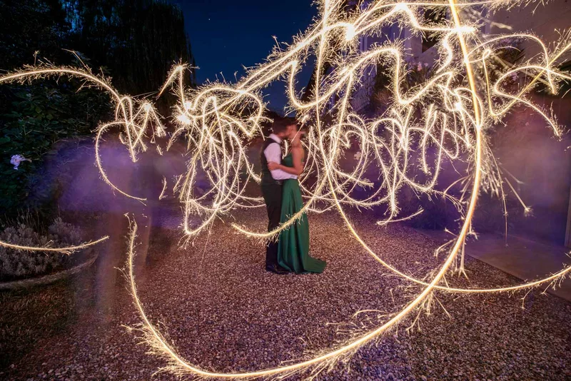 Coppia si abbraccia circondata da scintille luminose in un giardino durante la notte.