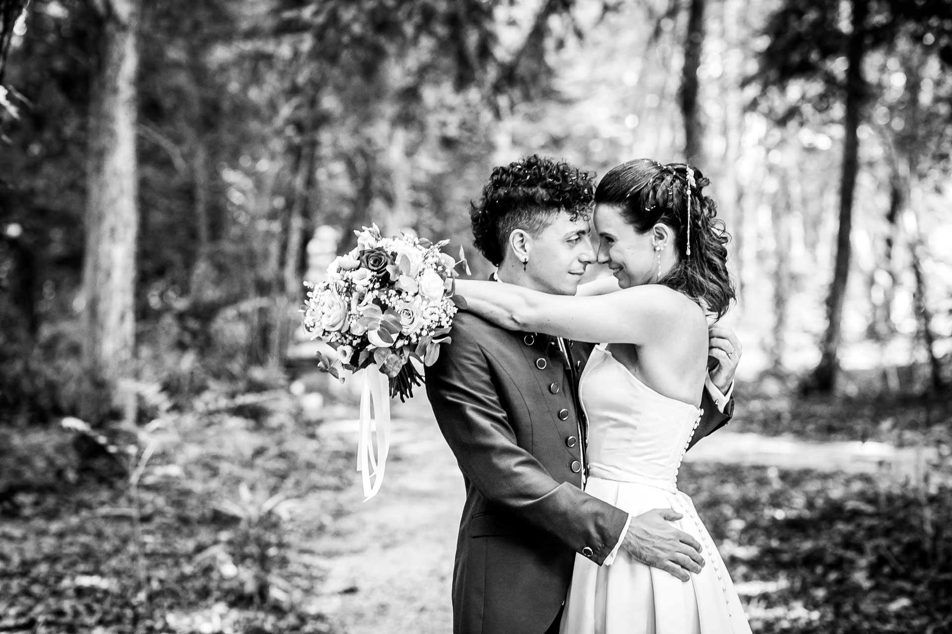 Coppia di sposi si abbraccia in un parco di Villa Luppis, circondati da alberi verdi, mentre la sposa tiene un bouquet di...